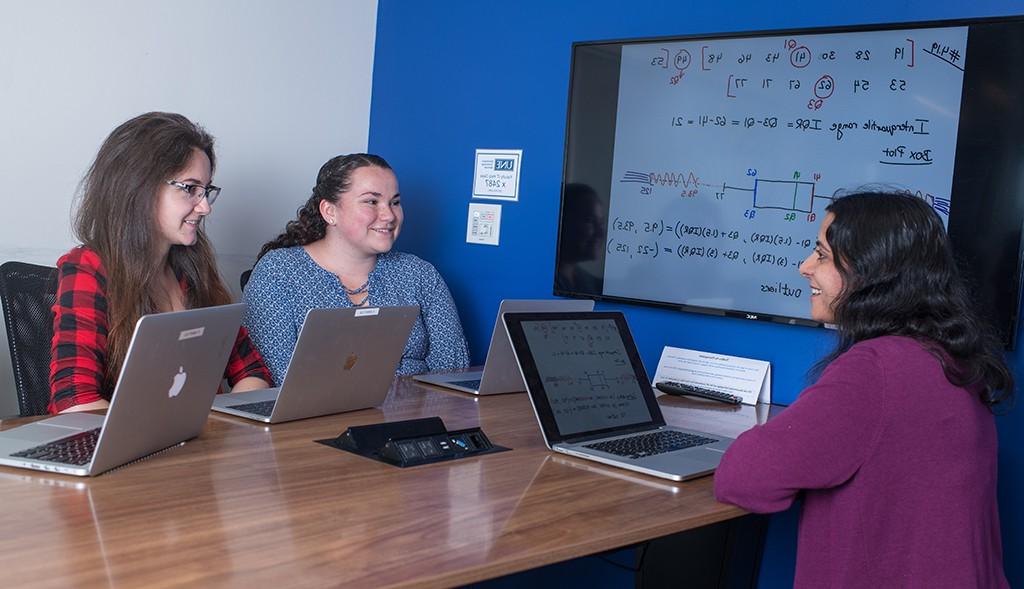 Three U N E students sit at a table with lap top computers