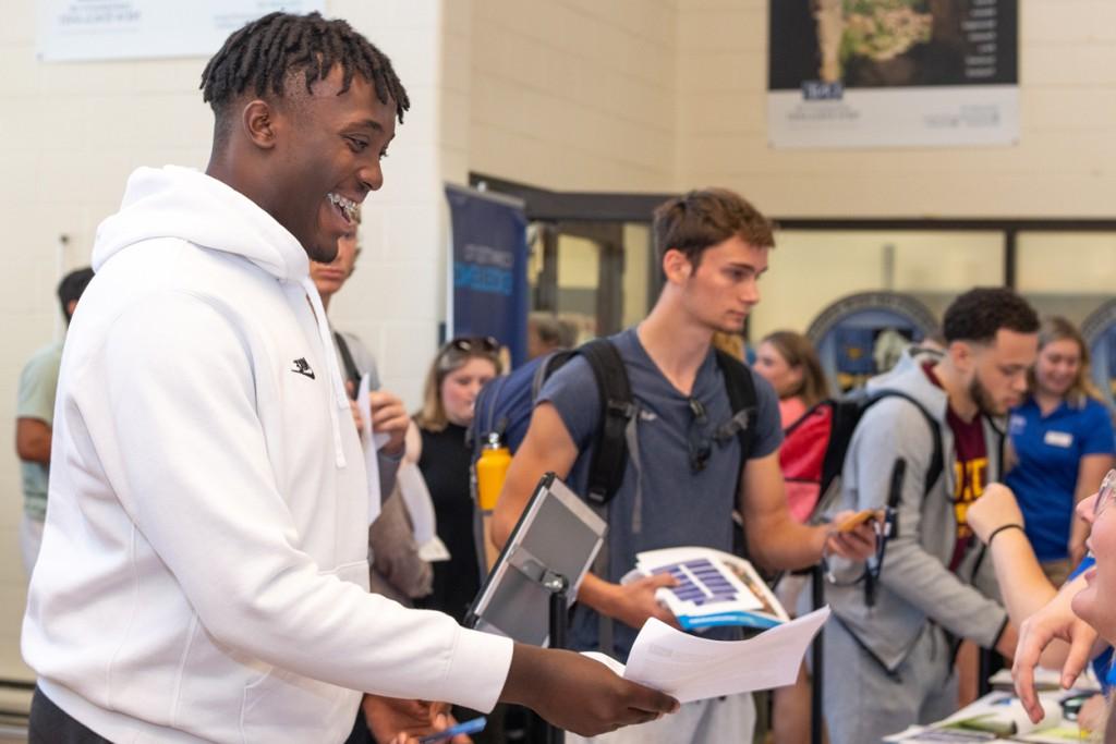 A new student happily passes orientation papers to a staff member